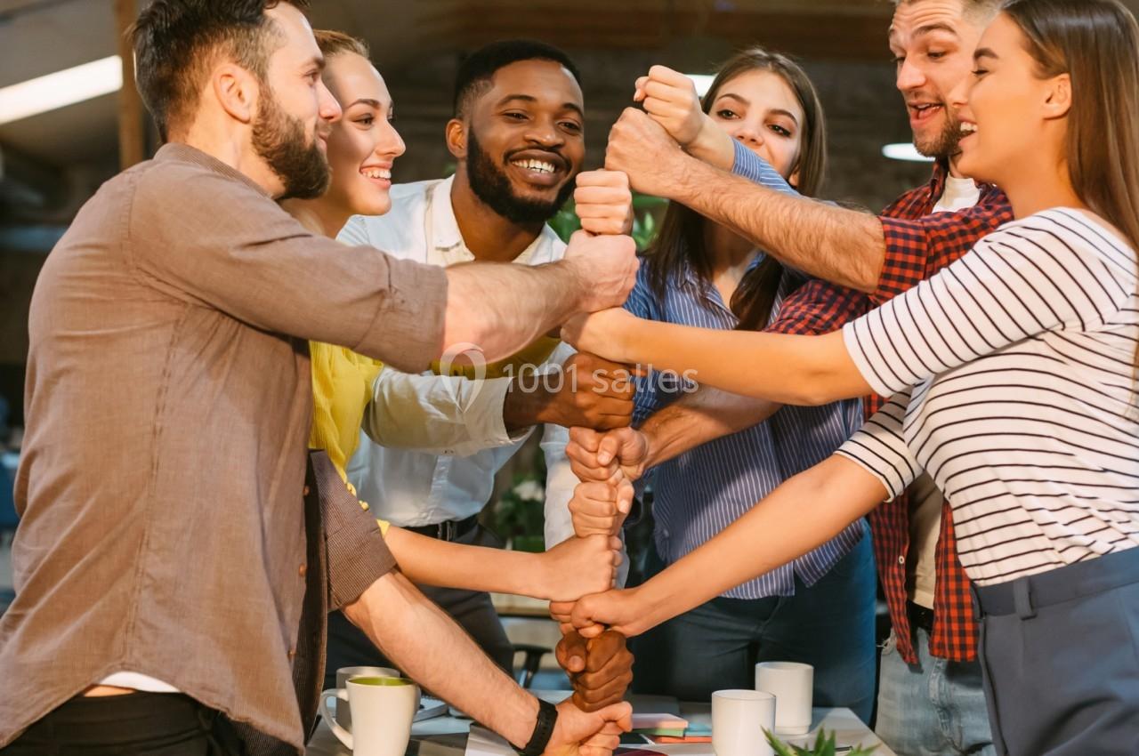 Un groupe de personnes souriantes se tient les mains en cercle dans un espace de travail collaboratif.