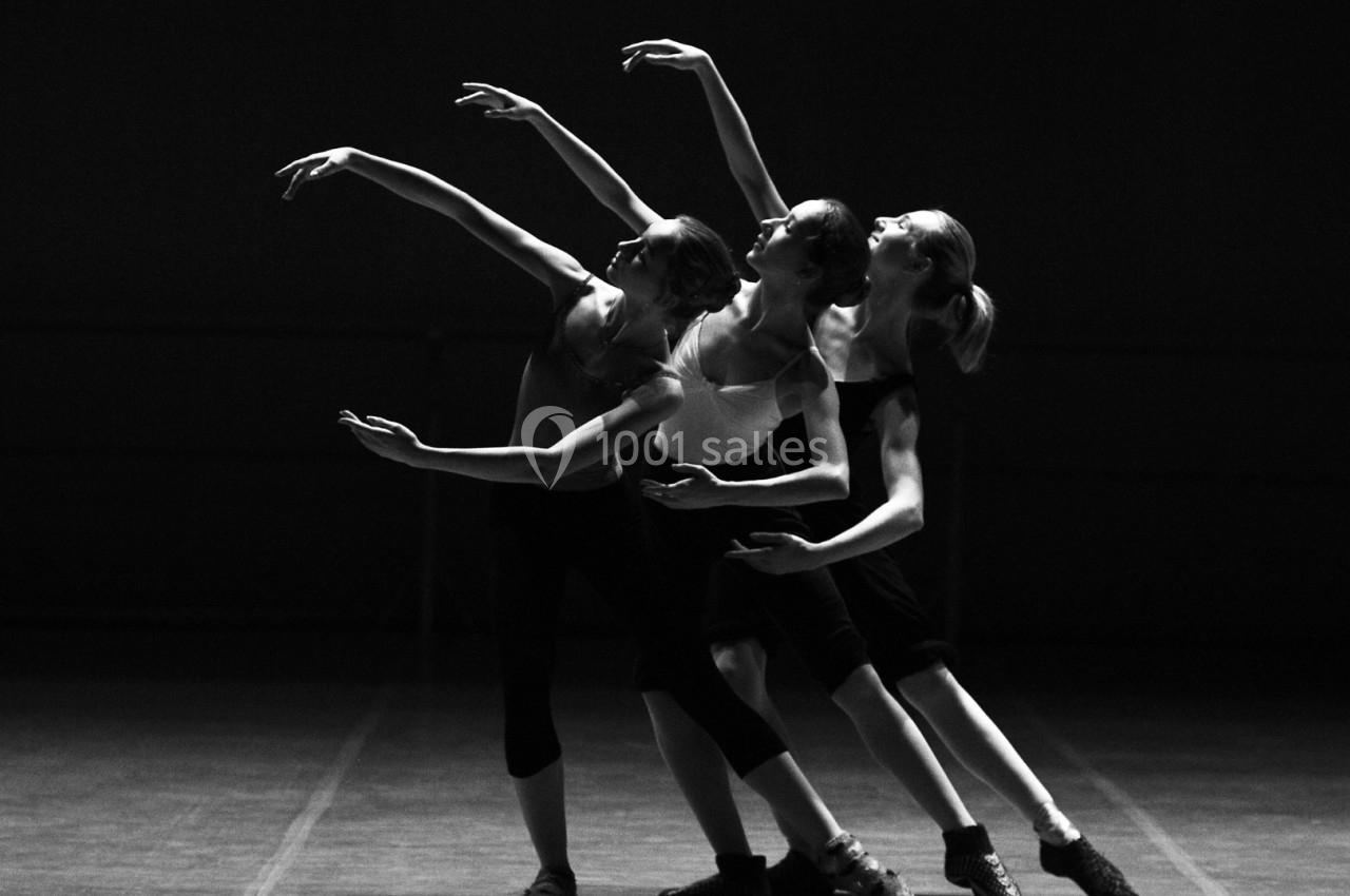 Trois danseuses exécutant une chorégraphie synchronisée sur une scène sombre, en noir et blanc.