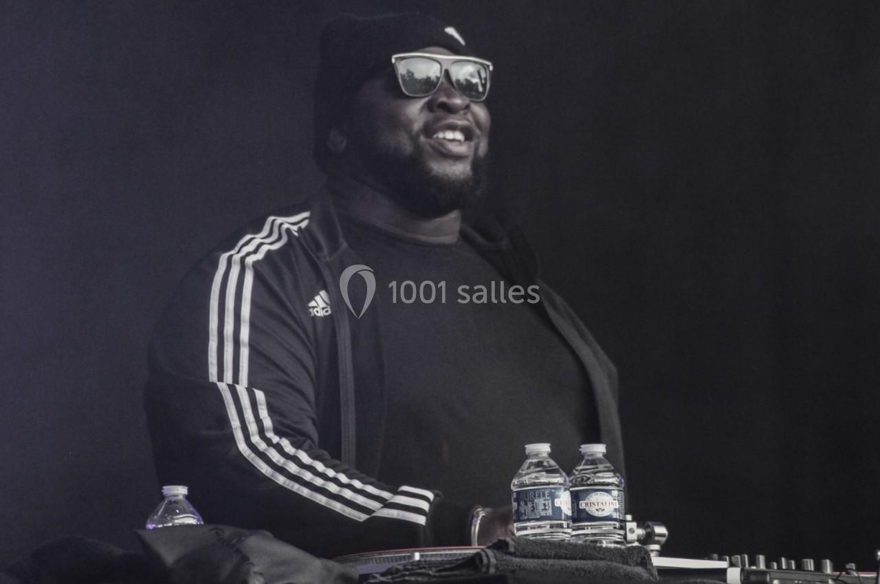 Un DJ portant des lunettes de soleil et un bonnet mixe sur scène avec des bouteilles d'eau posées devant lui.