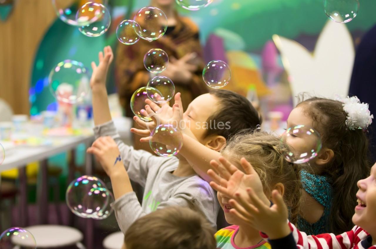 Des enfants jouent joyeusement avec des bulles de savon dans un espace coloré et animé.