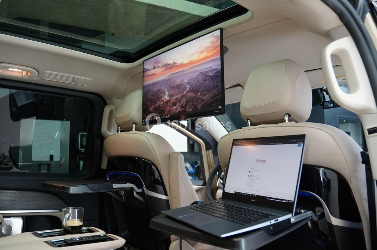 Intérieur d'un véhicule avec un ordinateur portable sur une table et un écran fixé au plafond affichant un paysage.