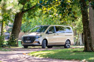 Façade d'un grand bâtiment de style classique avec des volets blancs, deux véhicules noirs et deux personnes devant.