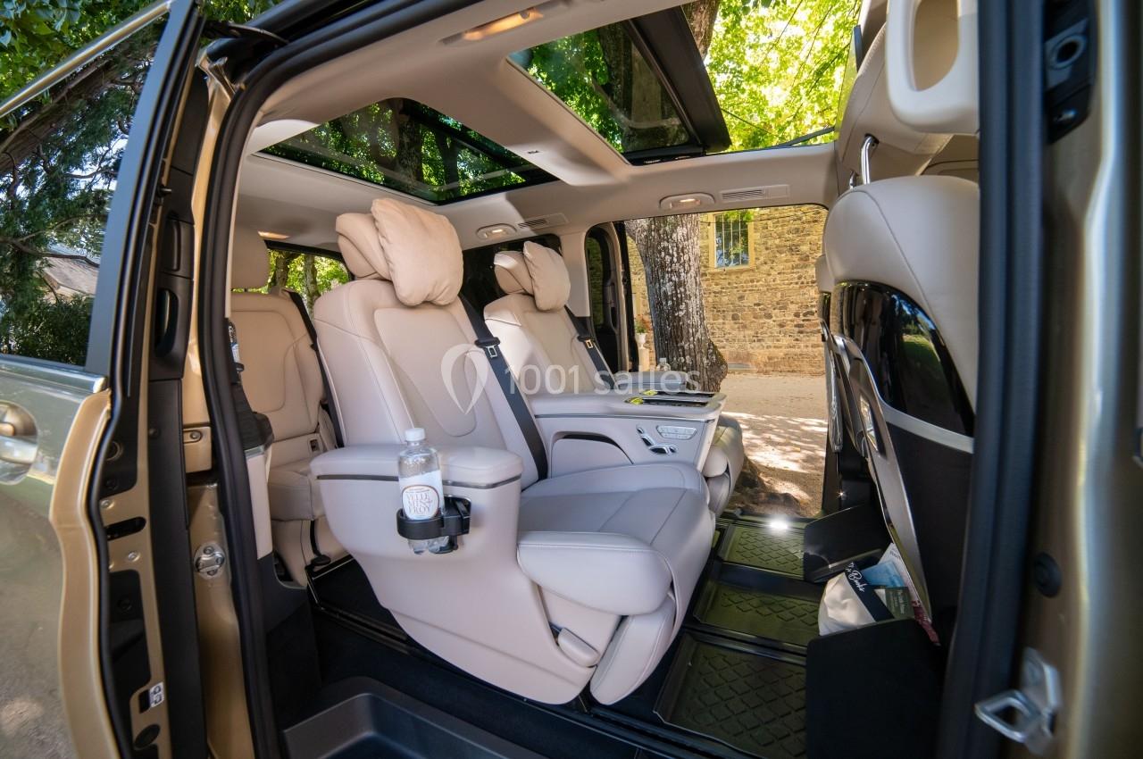 Vue intérieure d'un véhicule avec des sièges en cuir beige, accoudoirs et porte-gobelet, sous un toit panoramique.