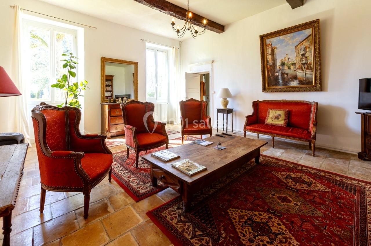 Salon lumineux avec mobilier ancien, fauteuils rouges, tapis orientaux, tableau encadré et grandes fenêtres.