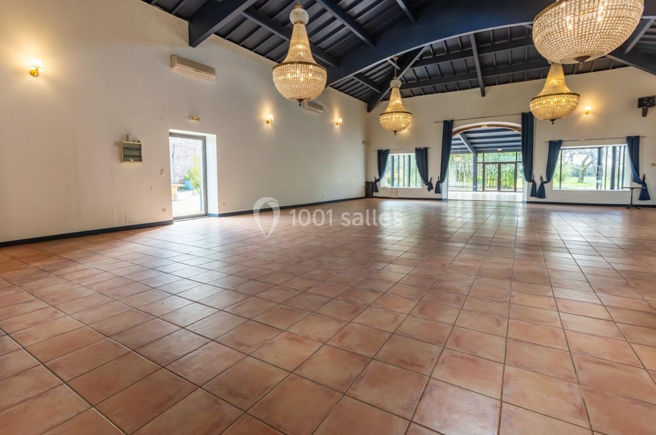 Salle spacieuse avec carrelage au sol, grandes baies vitrées, poutres apparentes et lustres suspendus.
