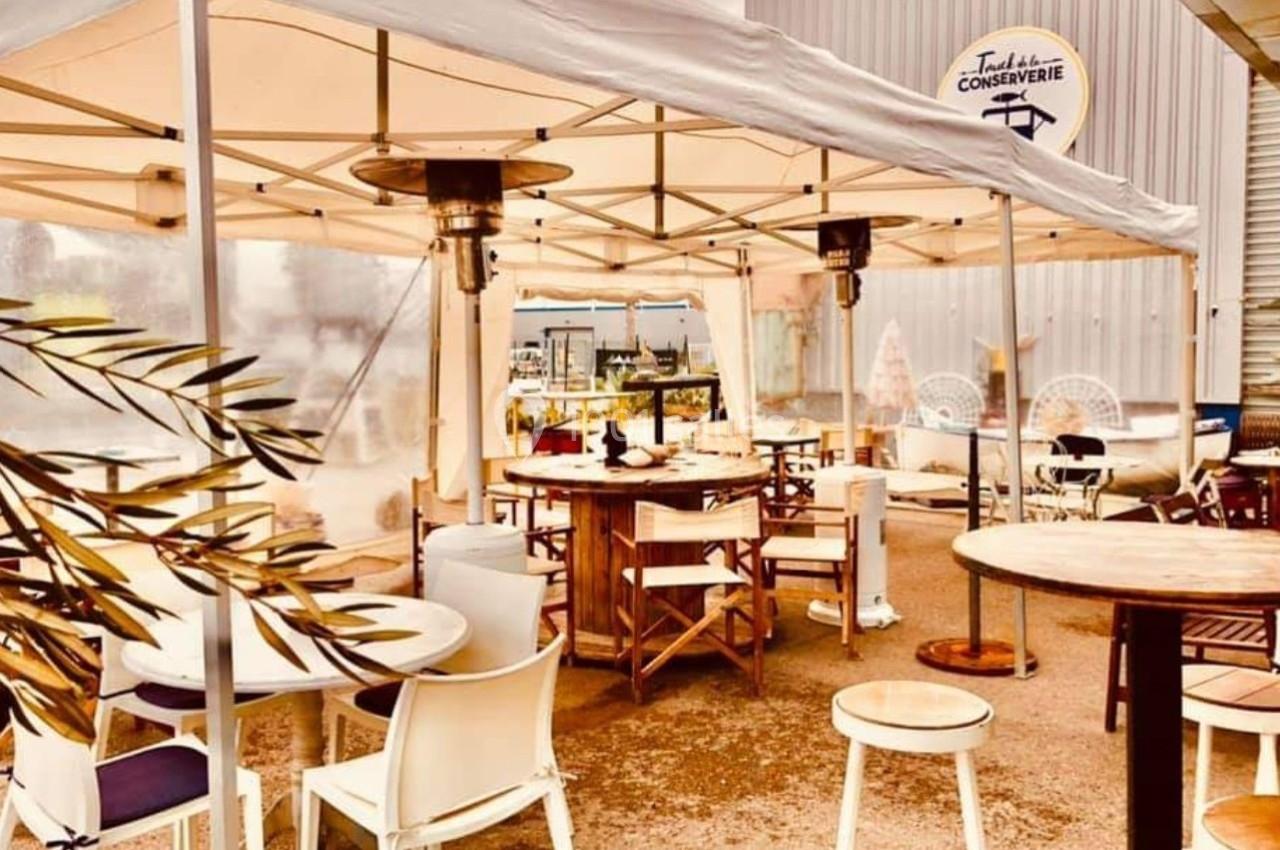 Terrasse extérieure couverte avec tables et chaises, entourée de décorations et d'un mur portant un logo industriel.