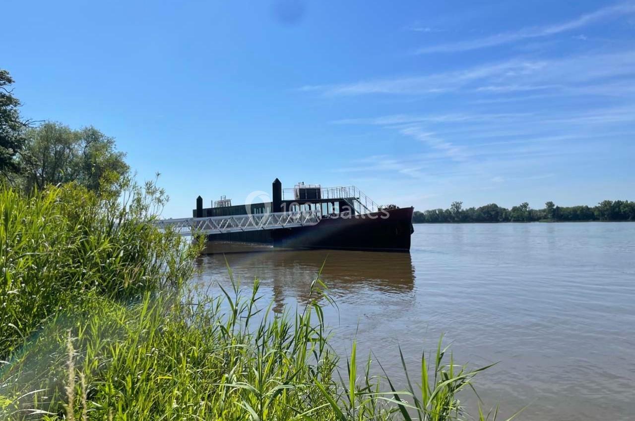 Bateau amarré près de la rive d'une rivière bordée de végétation sous un ciel bleu dégagé.