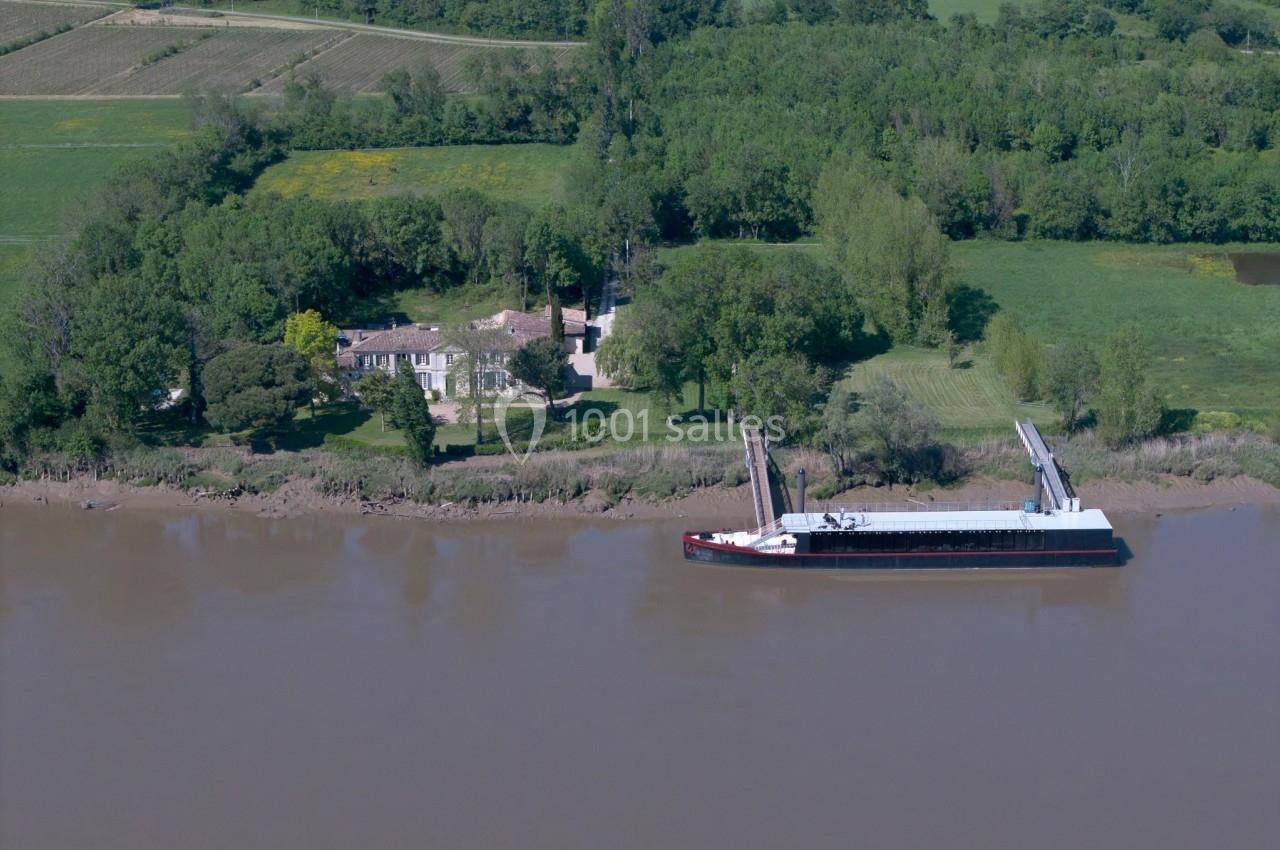 Vue aérienne d'une péniche amarrée sur une rivière près d'une propriété entourée de champs et d'arbres.