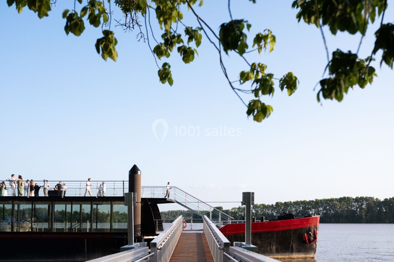 Un bateau amarré sur une rivière avec des passagers sur le pont, entouré d'arbres et d'un ciel dégagé.