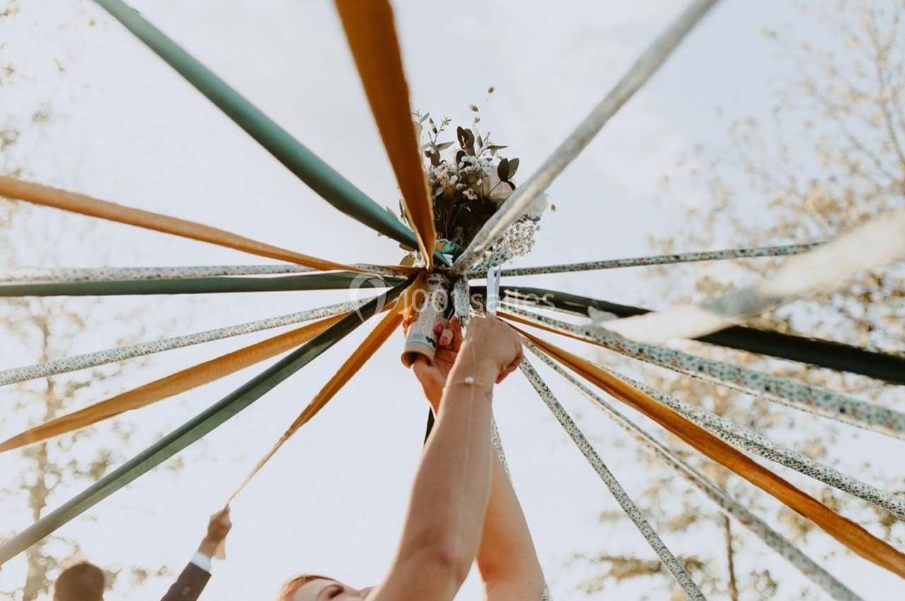 Des rubans colorés tendus vers un bouquet de fleurs tenu en l'air, avec un ciel clair et des arbres en arrière-plan.