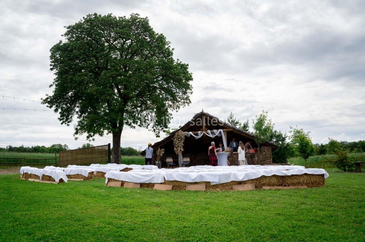 Un espace extérieur décoré pour un événement avec des bottes de foin recouvertes de tissu blanc et une cabane en arrière…