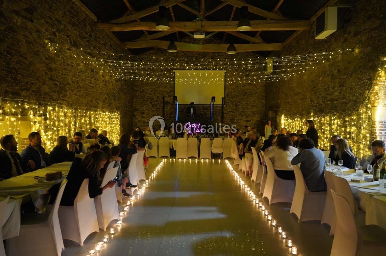 Salle de réception en pierre avec tables dressées, guirlandes lumineuses suspendues et éclairage chaleureux.