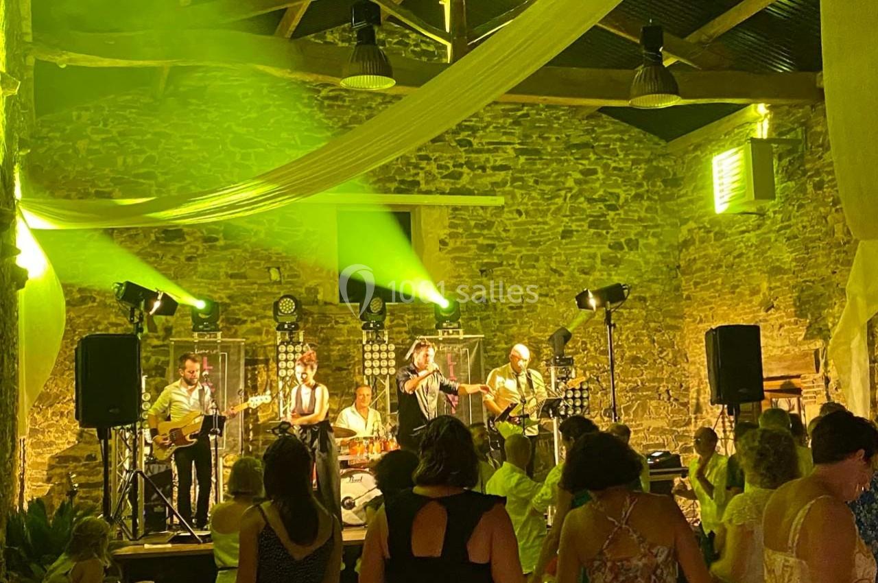 Groupe de musiciens jouant sur scène dans une salle en pierre illuminée, avec des personnes dansant au premier plan.