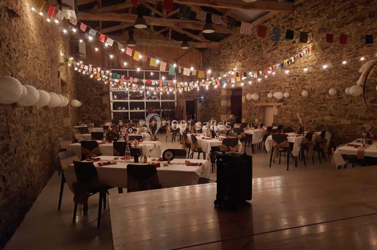 Salle en pierre décorée de guirlandes lumineuses et de fanions, avec des tables dressées pour un événement festif.