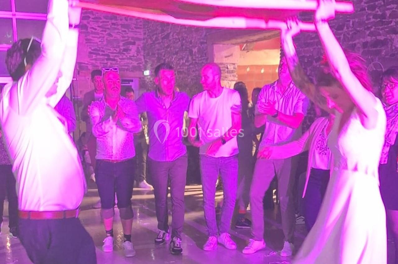 Des personnes dansent sous une lumière rose dans une salle en pierre, tenant un tissu en l'air.