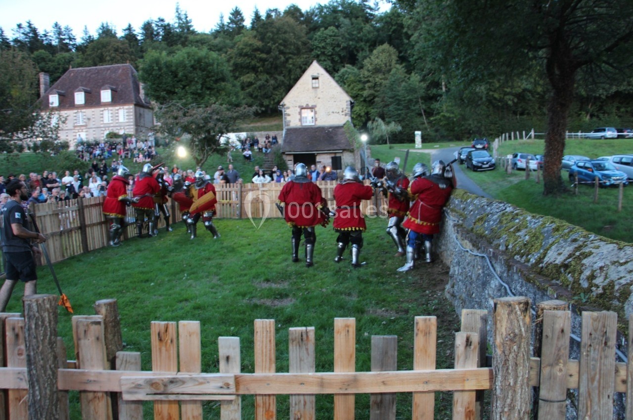 Des personnes en armures médiévales participent à une reconstitution historique dans un enclos en plein air.