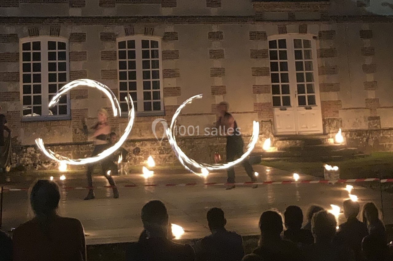 Deux artistes jonglent avec des objets enflammés devant un bâtiment en briques, sous les regards d'un public.