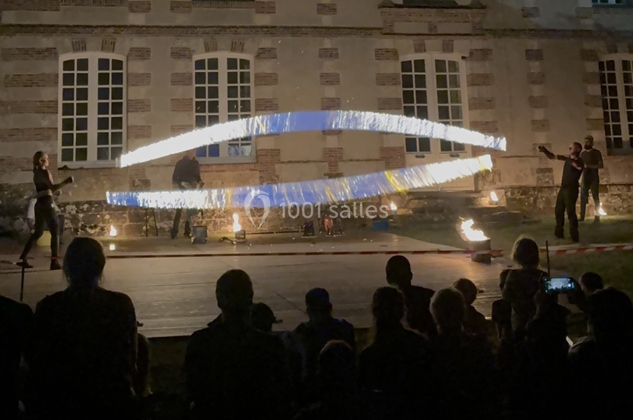Des artistes réalisent un spectacle de feu nocturne devant un bâtiment en pierre, sous les regards d'un public assis.