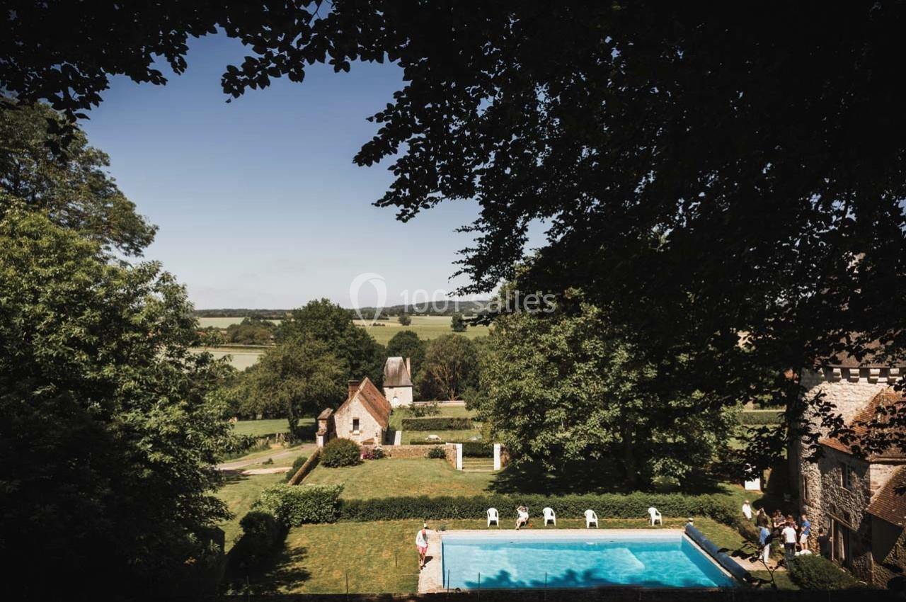 Vue d'un jardin avec piscine, entouré de bâtiments en pierre et de verdure, donnant sur une campagne vallonnée.