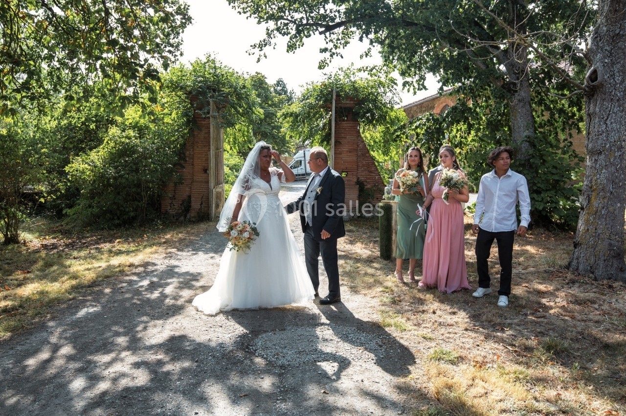 Une mariée en robe blanche marche aux côtés d'un homme en costume, suivie de demoiselles d'honneur et d'un invité, dans un…