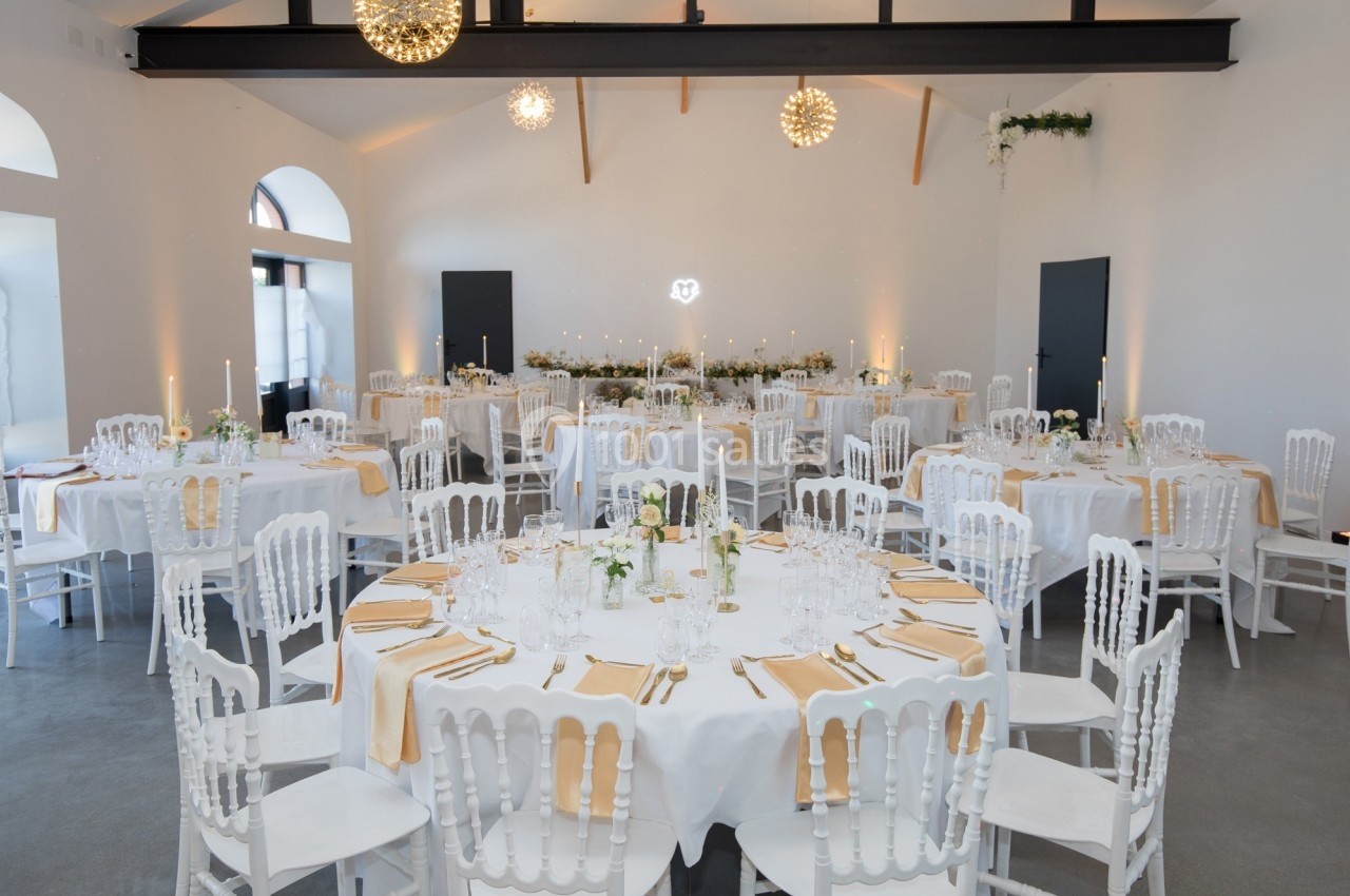 Salle de réception élégante avec tables rondes dressées, nappes blanches et décorations lumineuses suspendues.