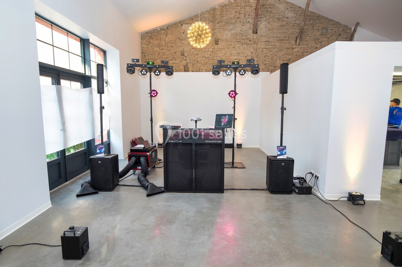 Installation de matériel de sonorisation et d'éclairage dans une salle avec murs blancs et plafond en poutres apparentes.