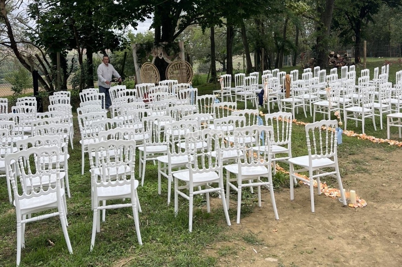 Chaises blanches disposées en rangées sur une pelouse pour une cérémonie en extérieur, avec décorations florales au sol.
