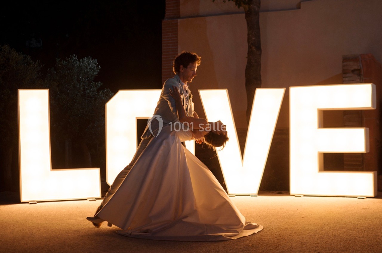 Un couple danse devant des lettres lumineuses formant le mot ’LOVE’ dans un décor extérieur nocturne.