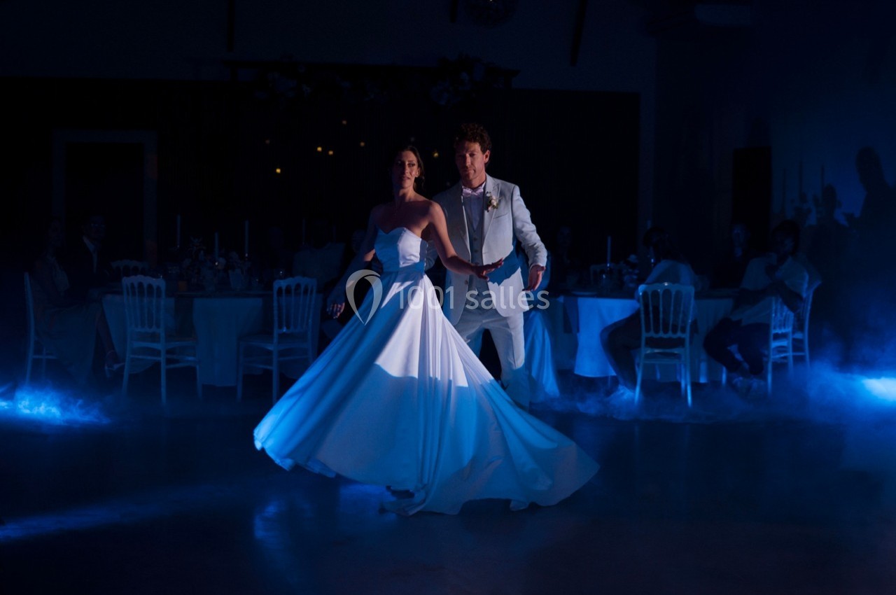 Un couple danse élégamment dans une salle faiblement éclairée, entourée de tables et d'une légère fumée au sol.