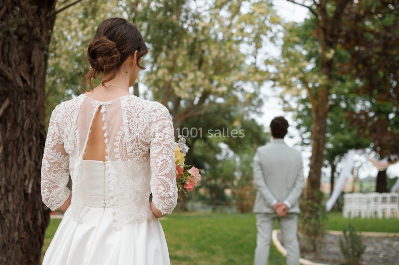 Une mariée en robe blanche regarde un homme en costume gris debout dans un jardin verdoyant.