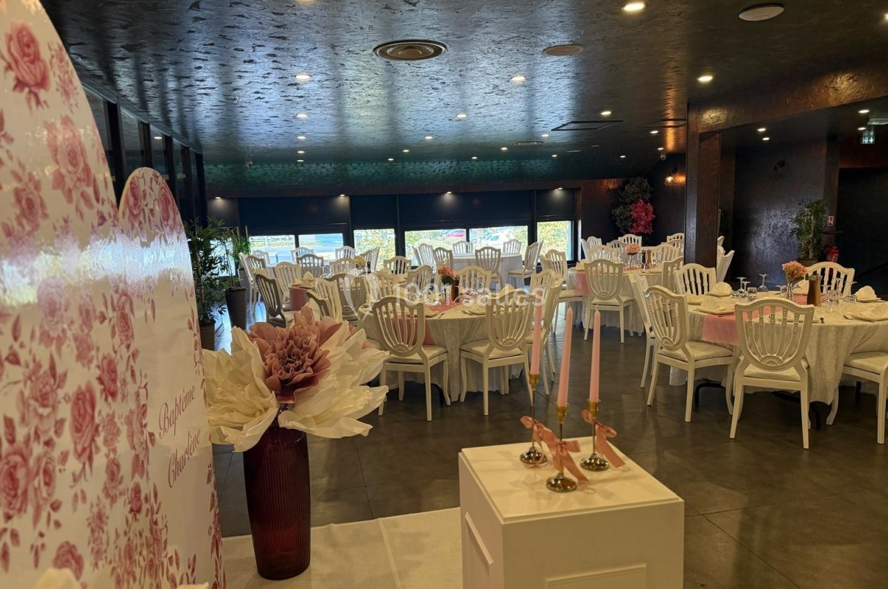 Salle de réception élégante avec tables dressées, chaises blanches et décorations florales dans une ambiance lumineuse.