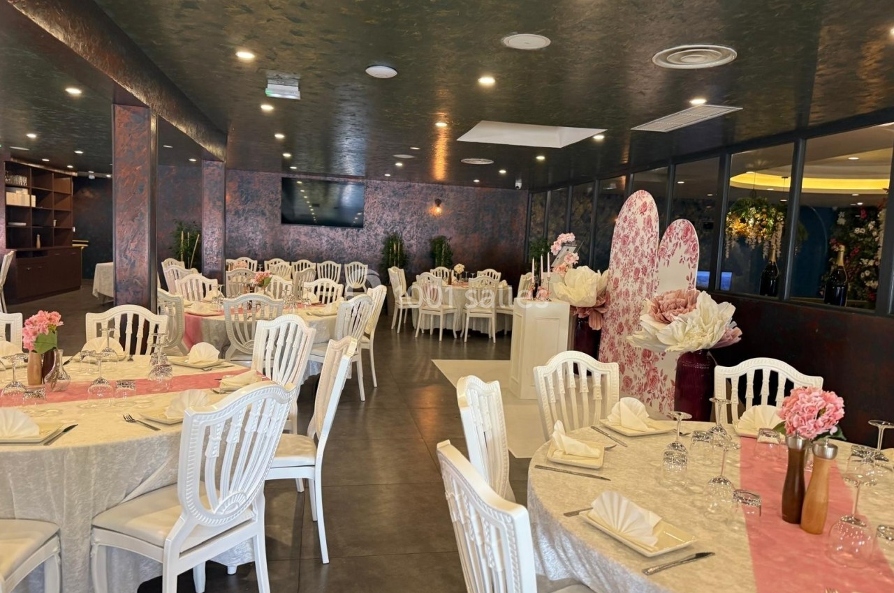 Salle de réception élégante avec tables décorées de nappes claires, chaises blanches et arrangements floraux roses.