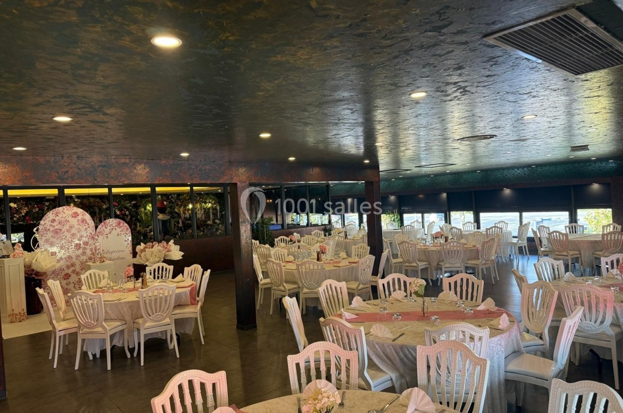 Salle de réception décorée avec des tables dressées, des chaises blanches et des éléments floraux.
