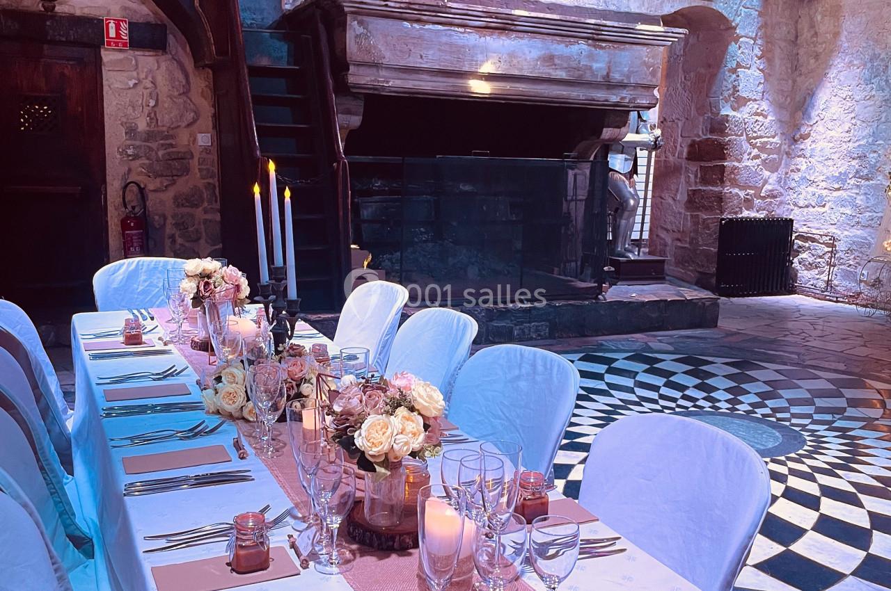 Table de réception élégamment dressée dans une salle en pierre avec cheminée, blason et bougies allumées.