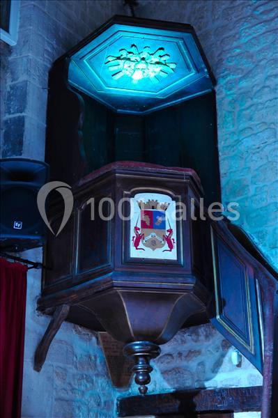 Chaire en bois sculpté avec armoiries, éclairée par une lumière bleue, dans un intérieur en pierre.