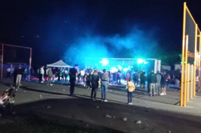 Foule dansante lors d'un événement nocturne en extérieur, éclairée par des lumières colorées.