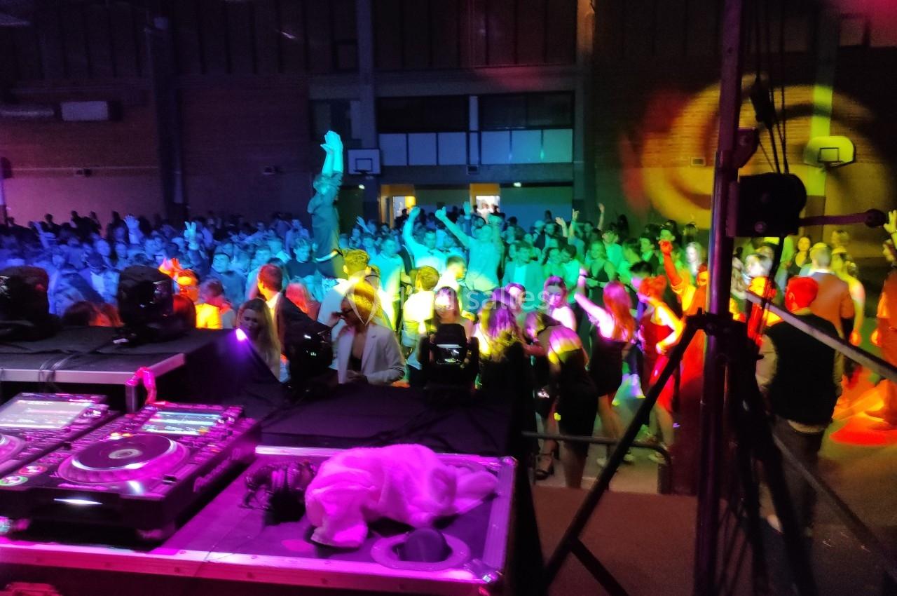 Vue d'une foule dansante sous des lumières colorées, prise depuis une scène avec une table de mixage au premier plan.