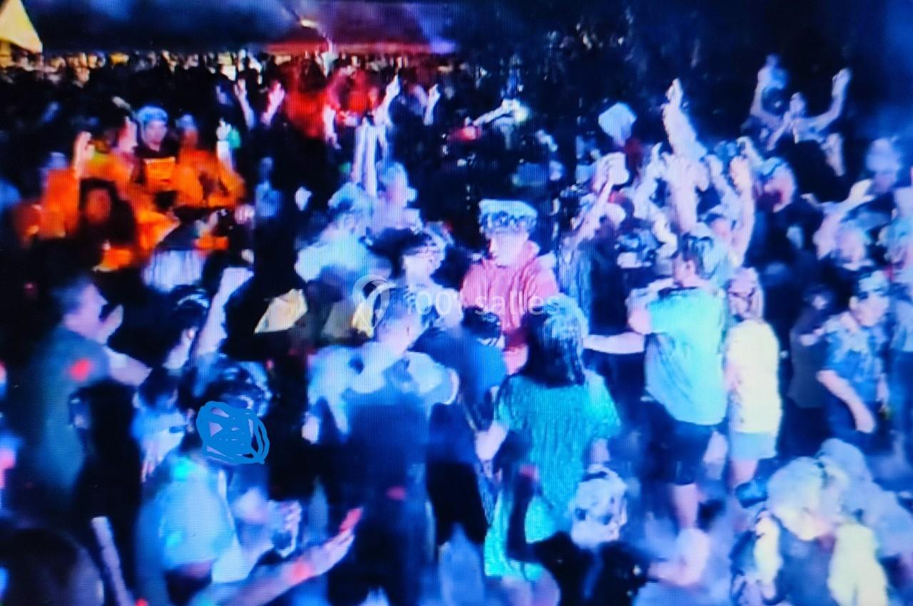 Foule dansante lors d'un événement nocturne en extérieur, éclairée par des lumières colorées.