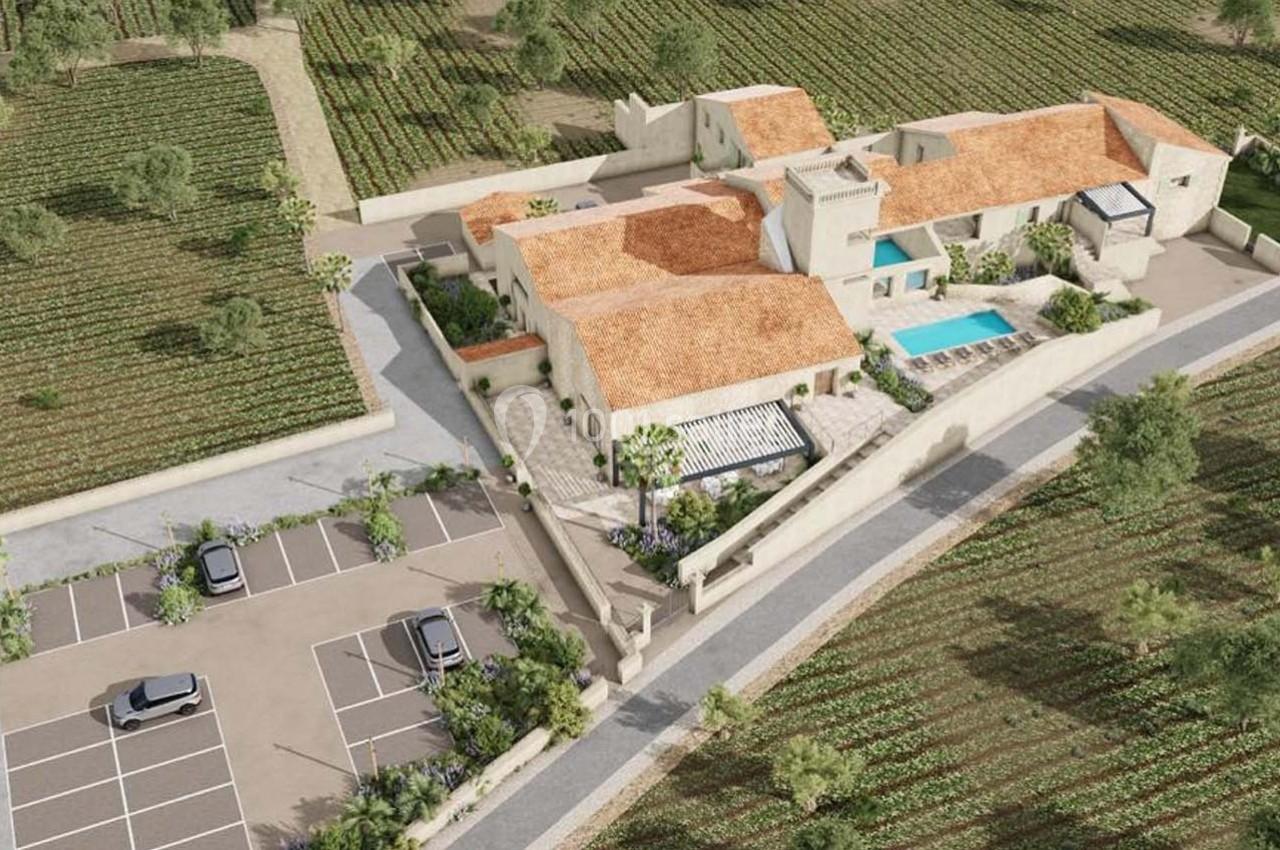Vue aérienne d'une propriété avec toits en tuiles, piscine, parking et entourée de vignes verdoyantes.
