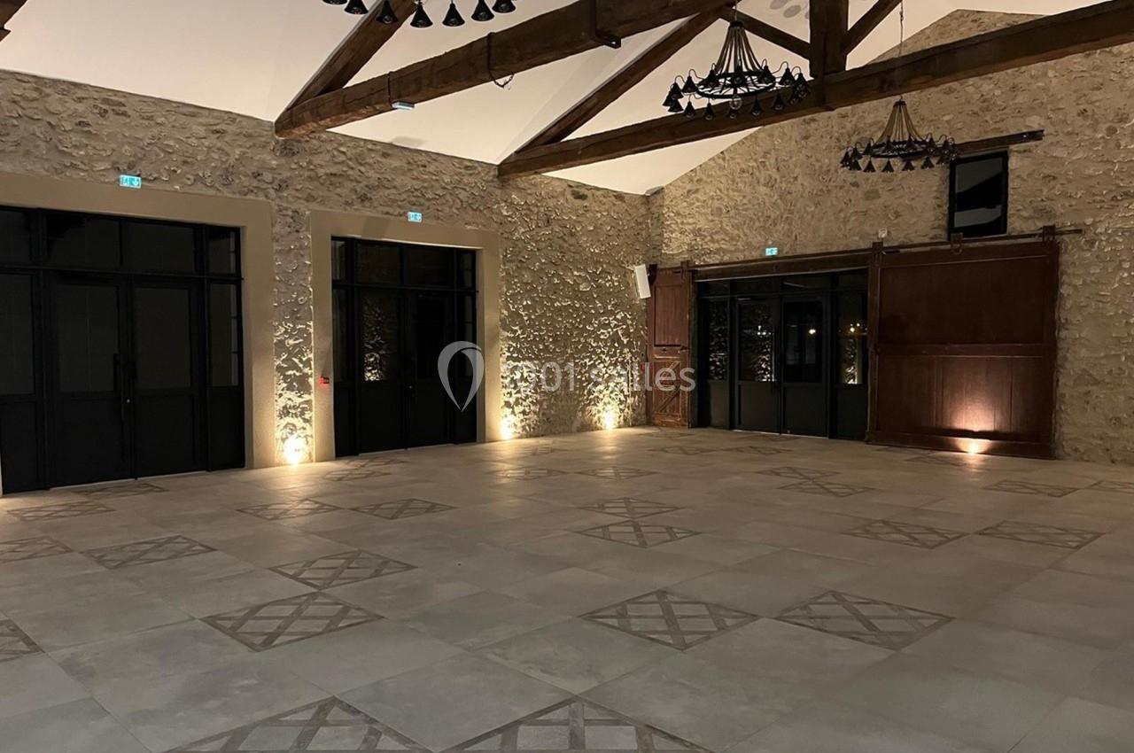 Salle spacieuse avec murs en pierre, poutres apparentes, sol carrelé et éclairage doux.