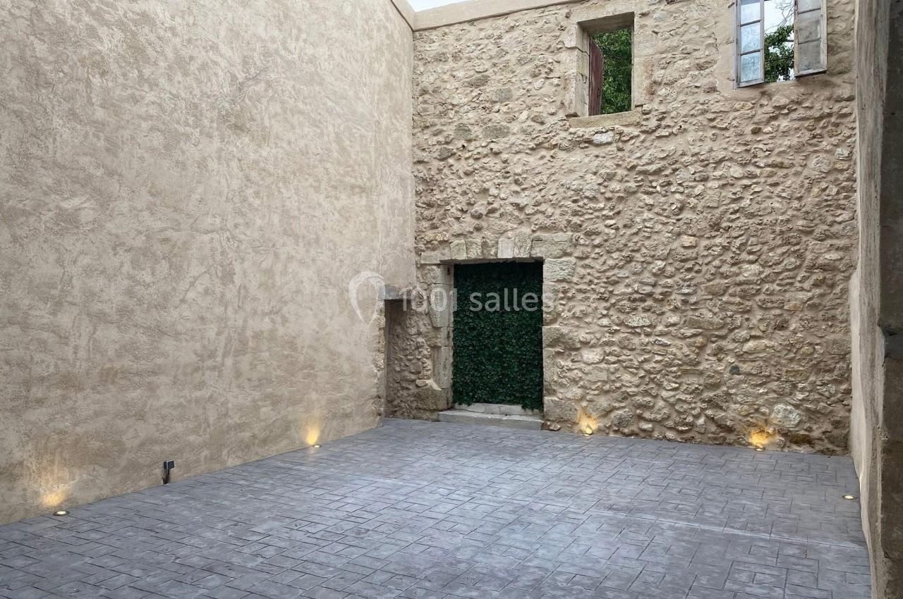 Cour intérieure en pierre avec un sol pavé, murs en pierre apparente, fenêtres et éclairage au sol.