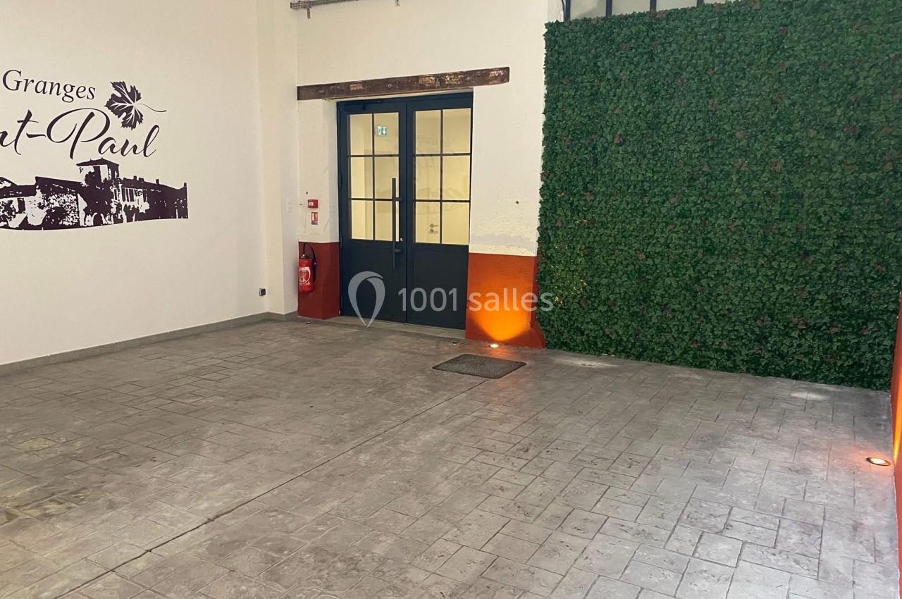 Entrée avec porte vitrée, mur végétal à droite, sol en béton et éclairage au sol.