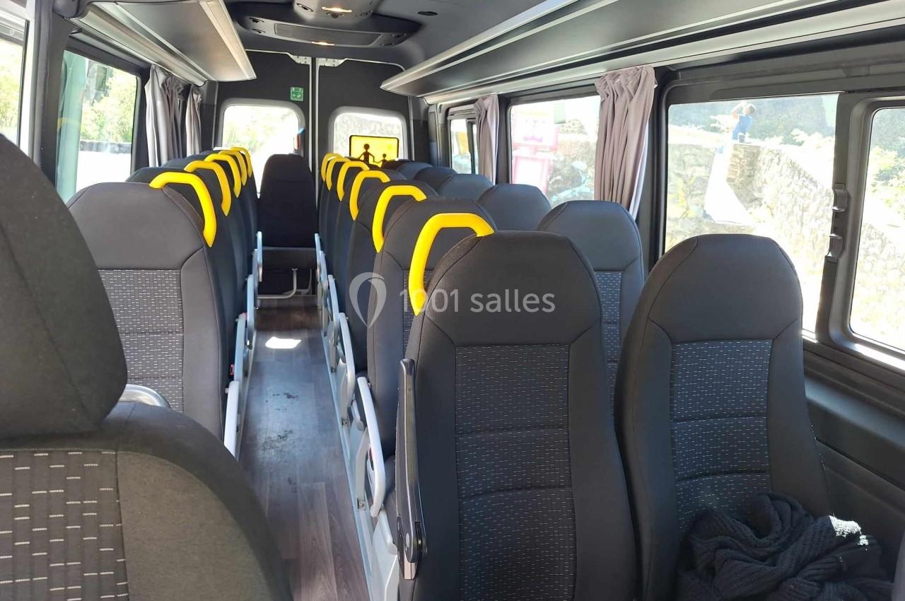 Intérieur d'un minibus avec des sièges noirs et appuie-têtes jaunes, rangés en deux colonnes.
