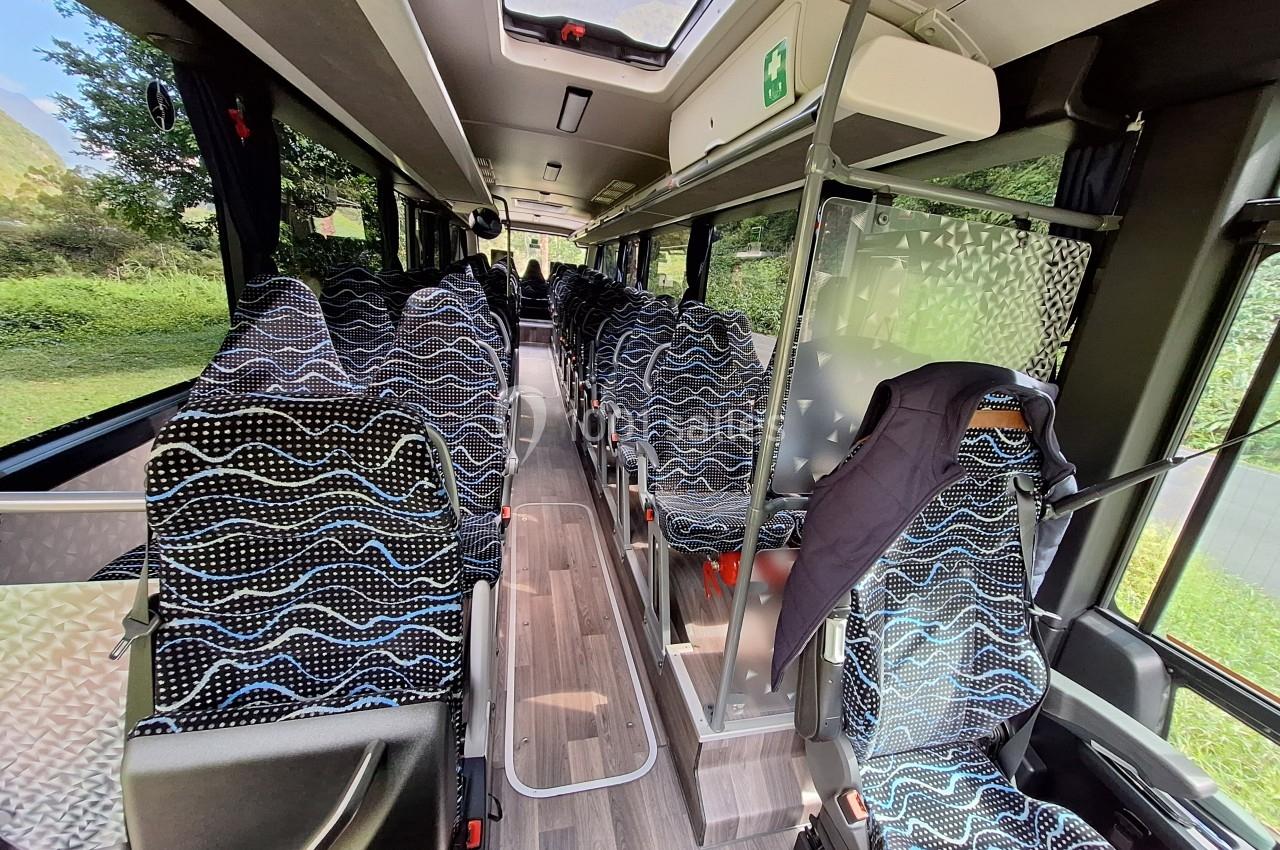 Intérieur d'un bus avec des sièges rembourrés à motifs, allée centrale et fenêtres offrant une vue sur la végétation…