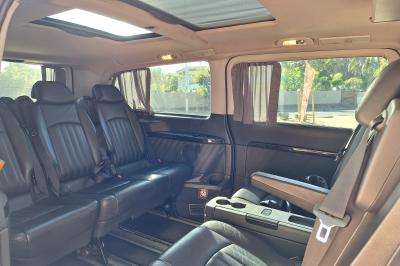 Intérieur d'un véhicule spacieux avec sièges en cuir noir, toit ouvrant et fenêtres équipées de rideaux.