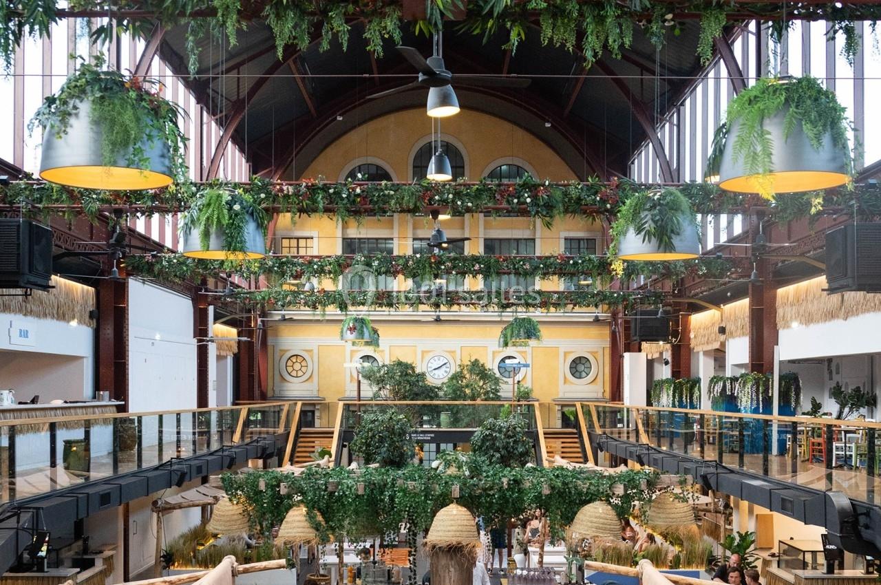 Intérieur d'un marché couvert avec une structure métallique, végétation suspendue et espaces aménagés sur deux niveaux.