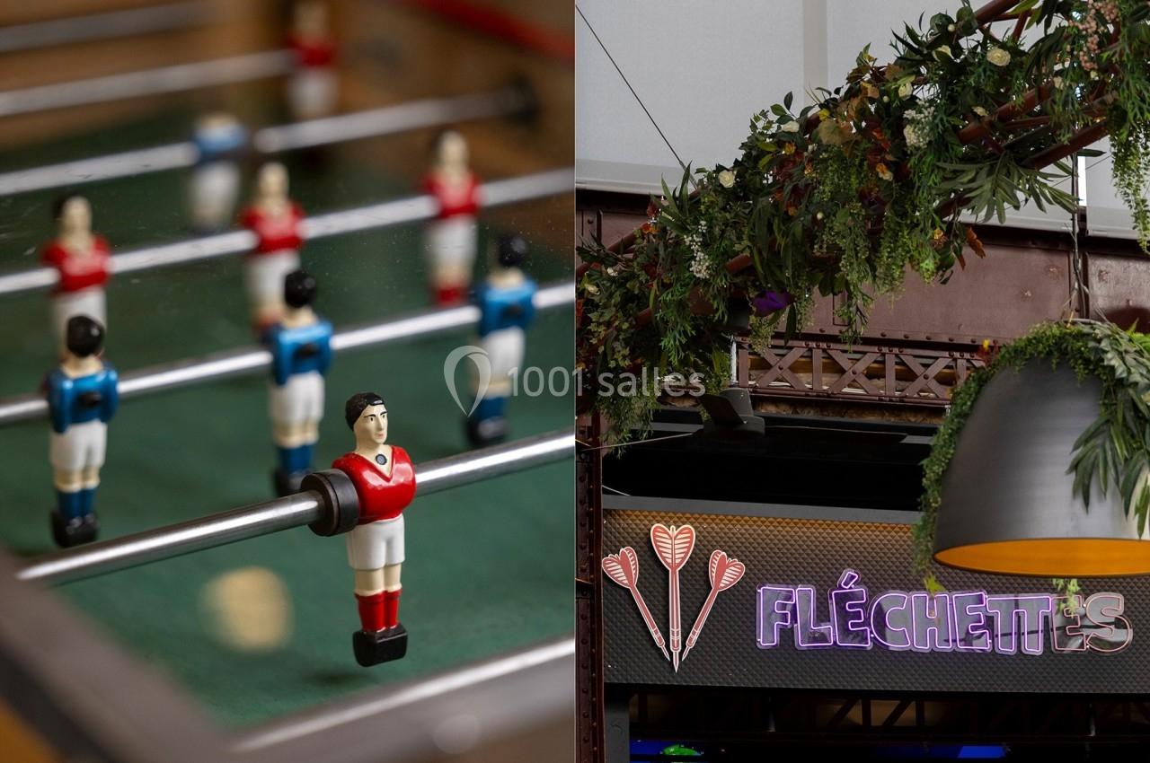 Joueurs miniatures d'un baby-foot à gauche et enseigne lumineuse ’Fléchettes’ avec décor végétal à droite.