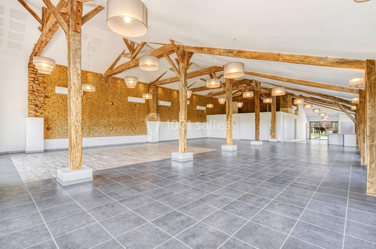 Salle spacieuse avec poutres en bois apparentes, murs en briques et sol en carrelage gris, éclairée par des suspensions…