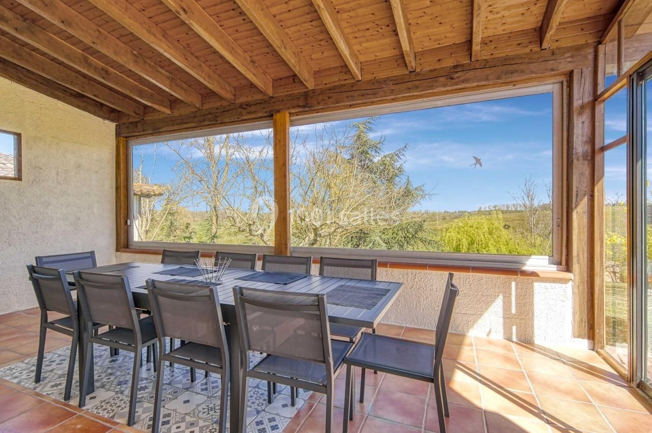 Salle à manger lumineuse avec table et chaises, grandes baies vitrées offrant une vue dégagée sur la nature.