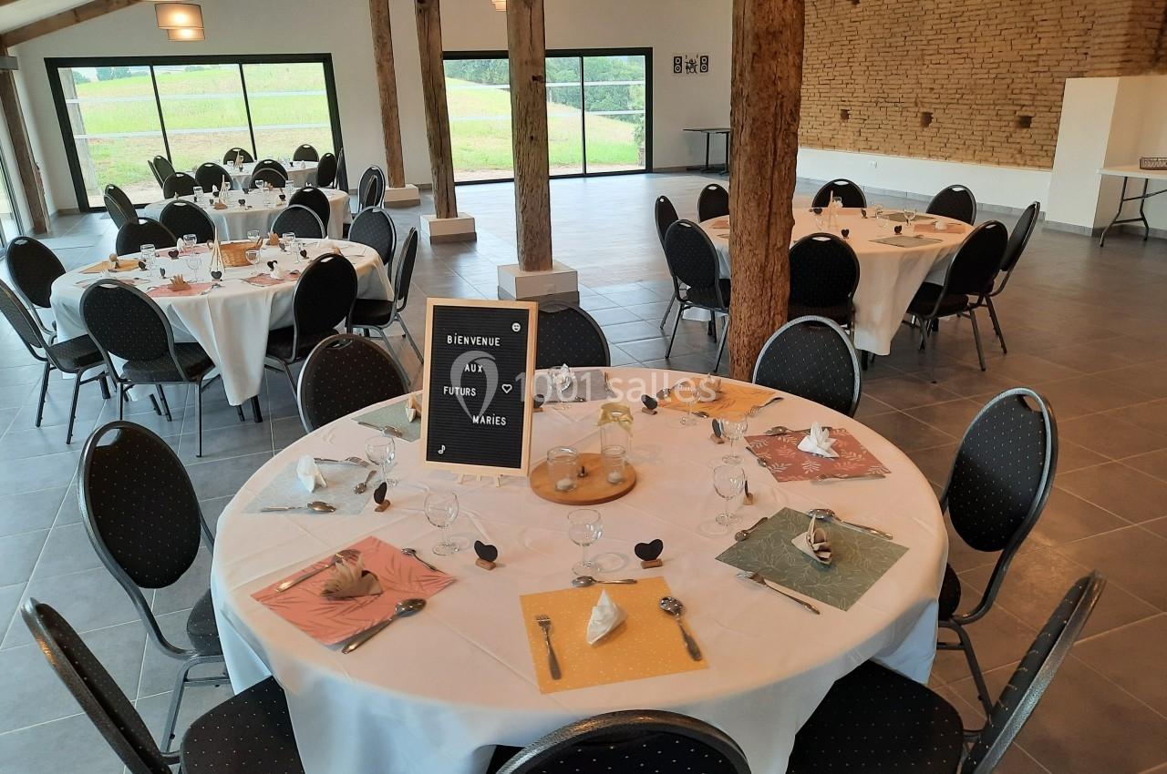 Salle de réception décorée pour un mariage, avec des tables rondes dressées et une pancarte de bienvenue.
